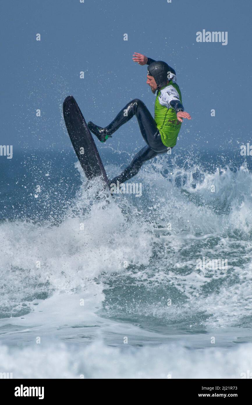Un surfeur mâle portant un casque de sécurité participant à une compétition de surf à Fistral à Newquay, en Cornouailles, au Royaume-Uni. Banque D'Images