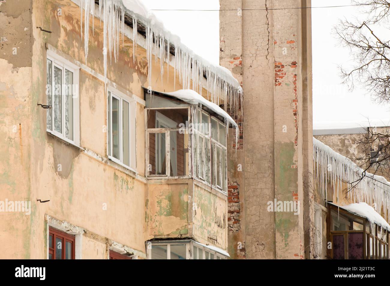 De grandes glaces pendent du bord du toit. Sur le fond du mur d'une ancienne maison en briques. Grandes cascades, même de belles rangées. Jour d'hiver nuageux, lumière douce. Banque D'Images