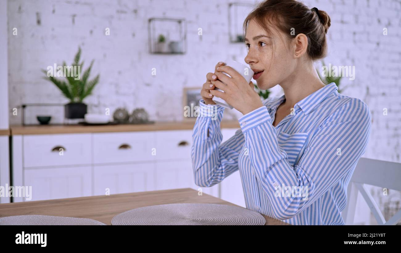 Une vue de la jeune femme portant une chemise rayée, assise dans la cuisine et buvant Banque D'Images
