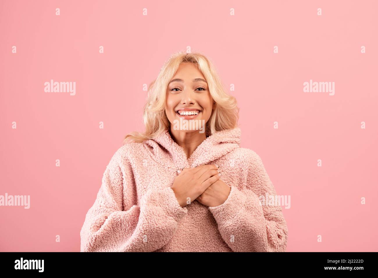 Une dame reconnaissante tient la main sur sa poitrine, exprimant sa gratitude, posant sur fond rose studio et souriant à la caméra Banque D'Images