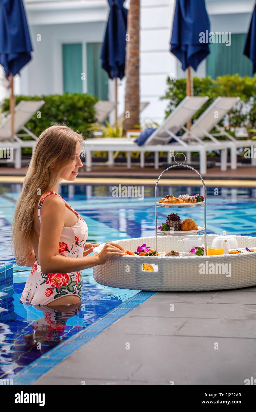 Femme en maillot de bain avec petit déjeuner flottant dans la piscine dans un hôtel de luxe Banque D'Images