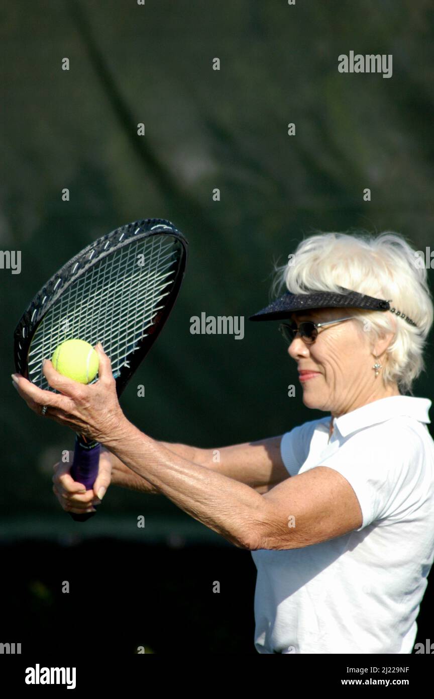 Femme joueur de tennis senior le faisant quotidiennement comme un hobby et pour s'amuser avec les cheveux blancs et la grande forme et le style à 70+ enseignement d'autres aînés Banque D'Images