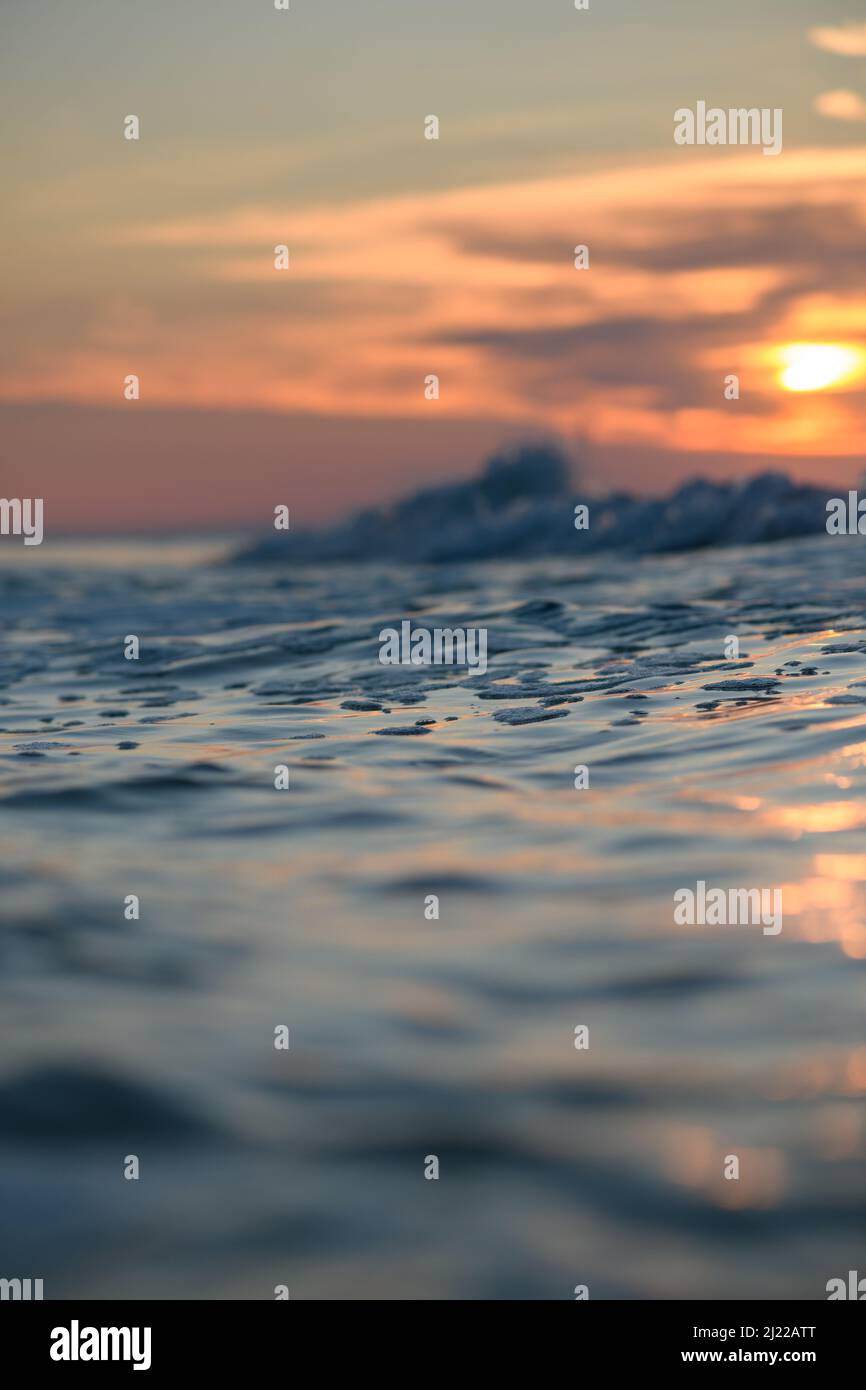 Gros plan de la surface de la mer contre le coucher du soleil. Photo verticale, point de prise de vue faible. Vagues de mer au premier plan. Banque D'Images