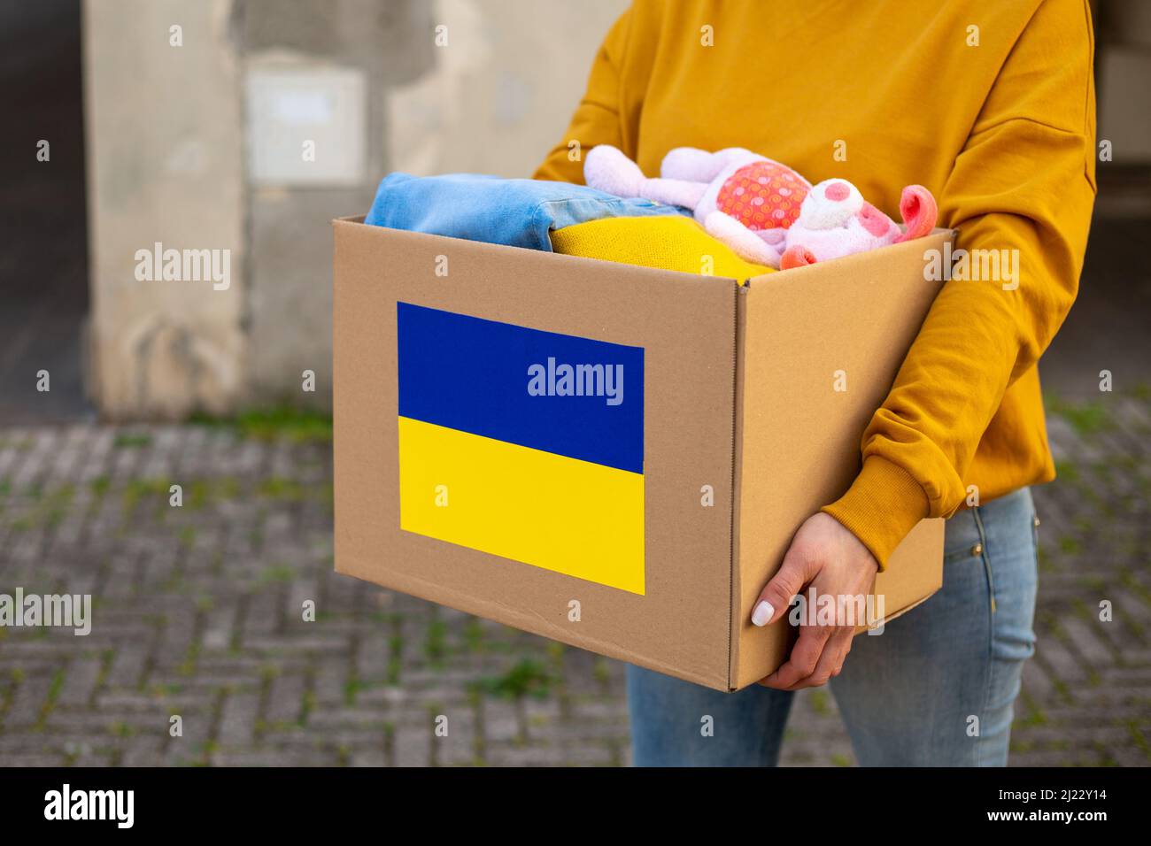 Les volontaires tiennent dans leurs mains une boîte d'aide humanitaire avec des choses et des jouets pour enfants pour les besoins des Ukrainiens dans la rue. Aide pour l'Ukraine Banque D'Images
