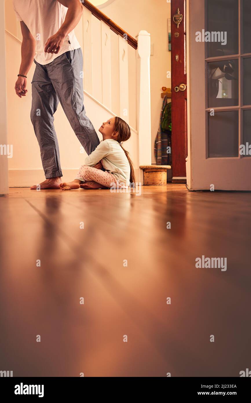 N'allez pas à papa. Photo d'une petite fille gaie qui attrate sa jambe de papas et ne laisse pas aller tout en étant assise sur le sol à la maison. Banque D'Images