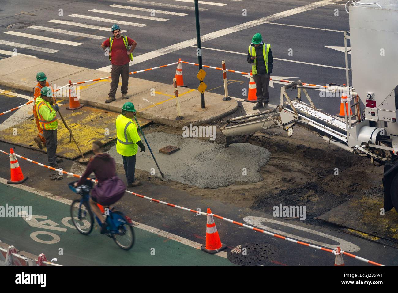 Les travailleurs versent du ciment sur une excavation de la chaussée après avoir terminé des travaux souterrains sur la neuvième avenue à Chelsea, à New York, le samedi 19 mars 2022.(© Richard B. Levine) Banque D'Images