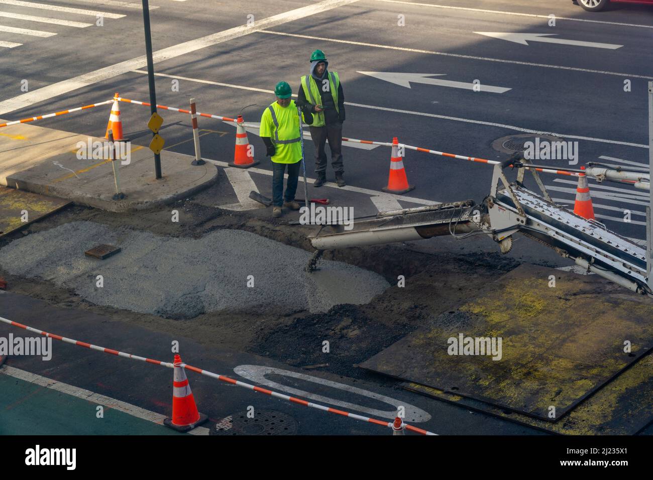 Les travailleurs versent du ciment sur une excavation de la chaussée après avoir terminé des travaux souterrains sur la neuvième avenue à Chelsea, à New York, le samedi 19 mars 2022.(© Richard B. Levine) Banque D'Images