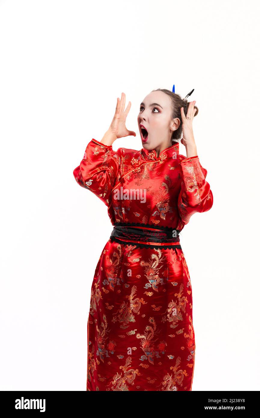Jeune femme vêtue d'un costume traditionnel chinois rouge, avec un petit pain dans ses cheveux tenu en place avec des stylos, levant ses mains sur son visage et avec un Banque D'Images