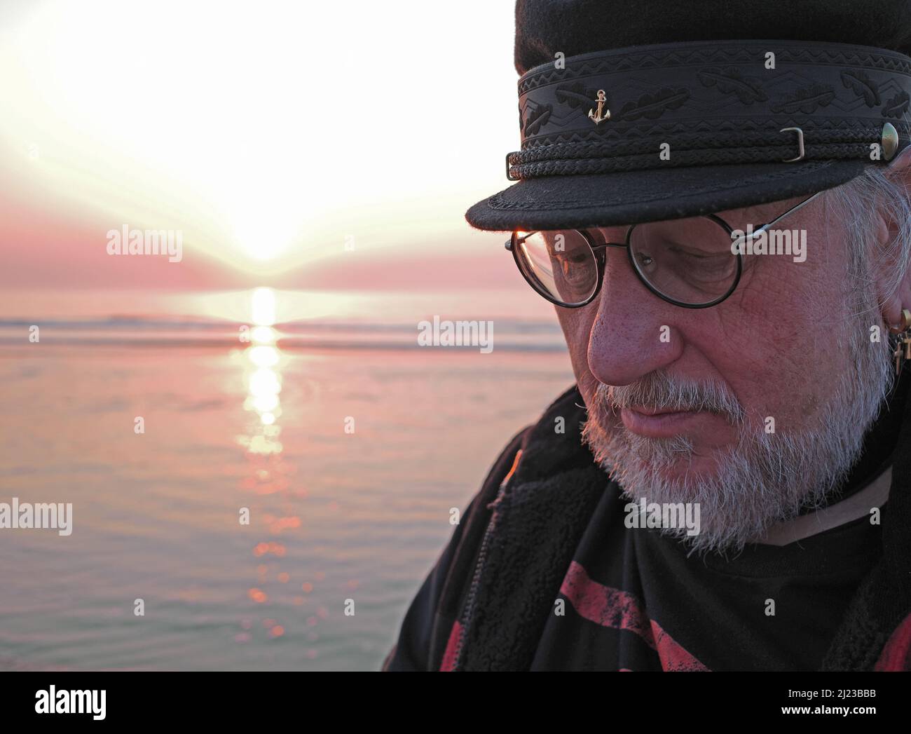 Le vieil homme et la mer au coucher du soleil. Un homme âgé regarde avec attention. L'homme a une barbe blanche et une casquette de marin sur sa tête Banque D'Images