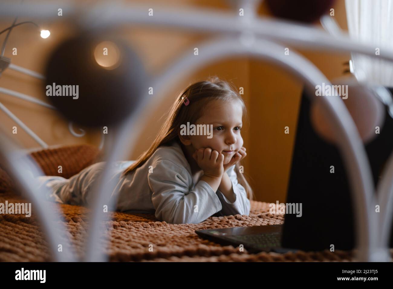 Enfants regardant des dessins animés sur un ordinateur portable. Enfant sérieux avec la technologie à la maison sur le lit passer du temps en ligne. Éducation et divertissement pour les tout-petits. Une fille Banque D'Images