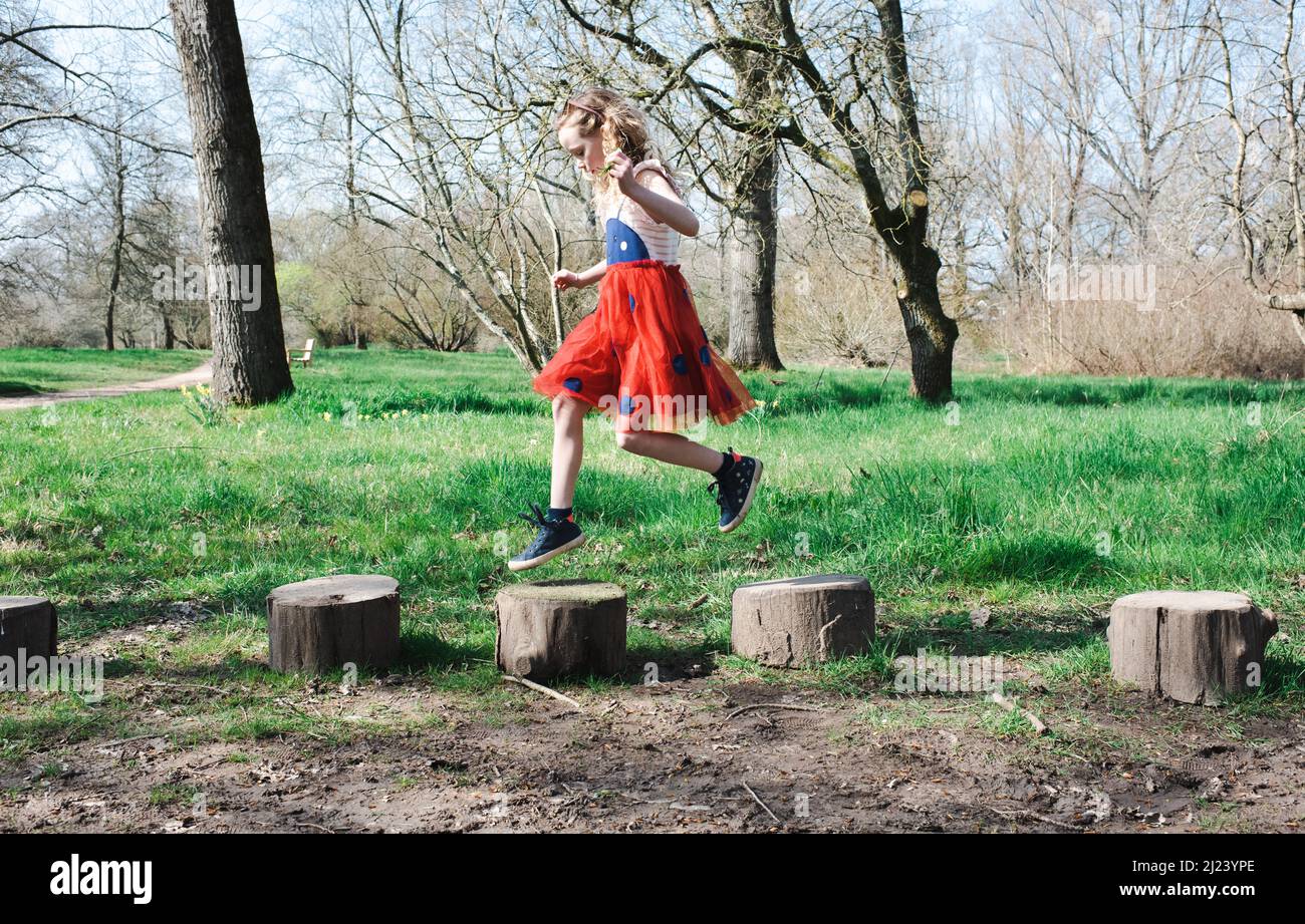 fille sautant sur des bûches au parc dans une robe Banque D'Images