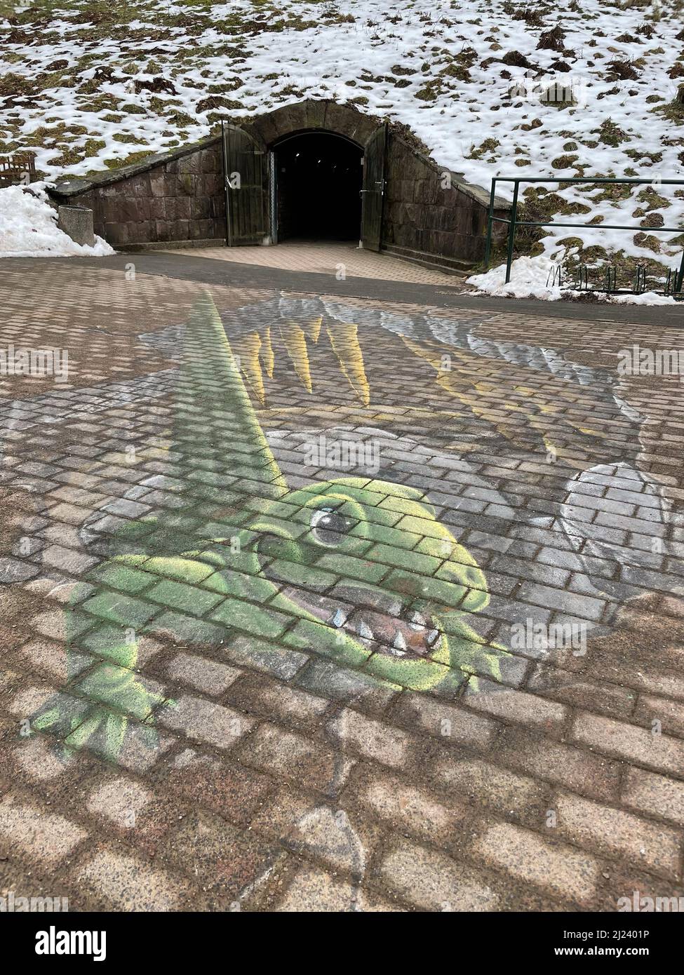 Plan vertical d'un dessin à la craie d'un dinosaure sur un sol devant une entrée de grotte Banque D'Images