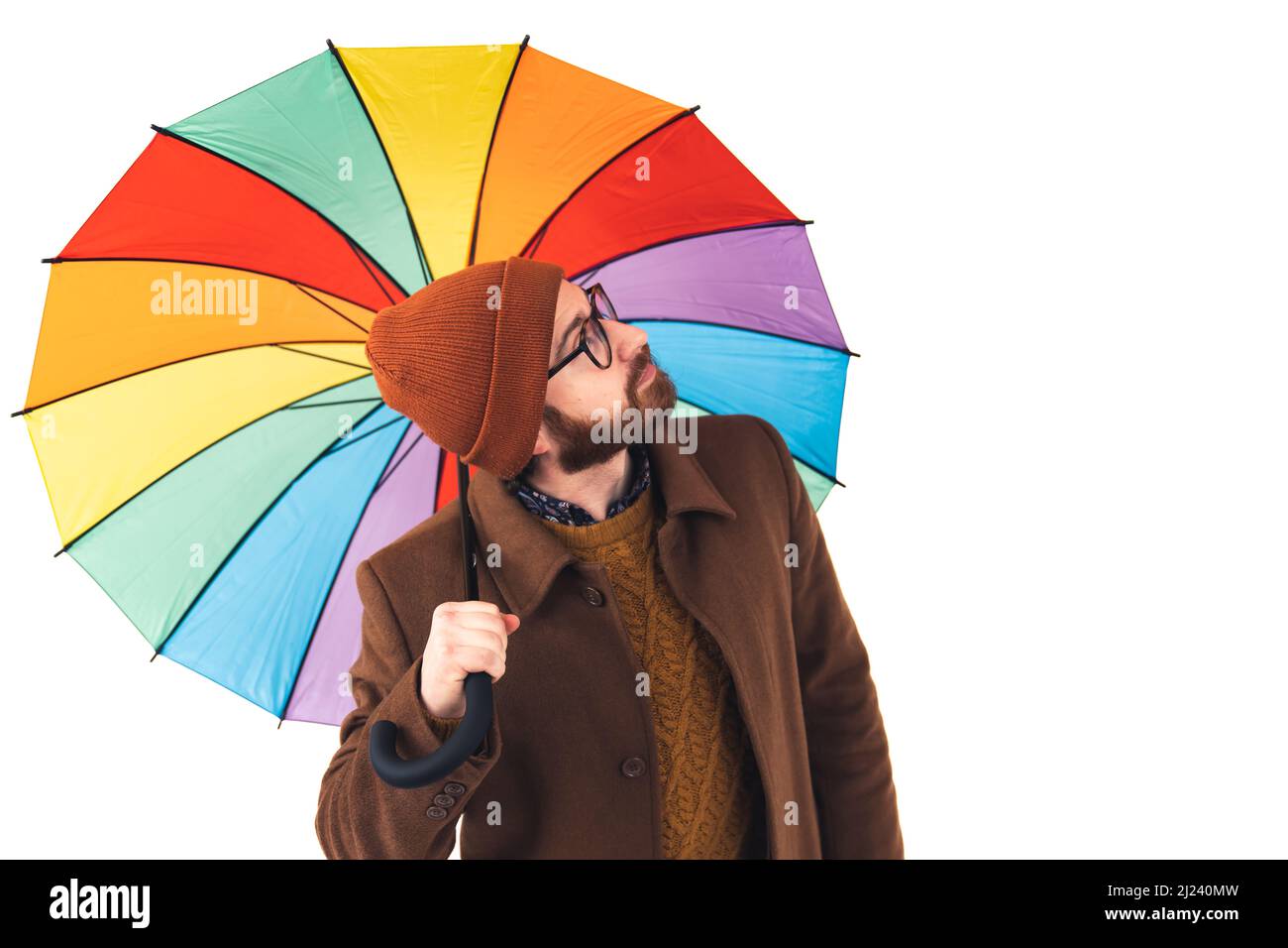 Portrait d'un jeune beau barbu caucasien homme tenant un parapluie multicolore et regardant vers le haut le ciel prévisions météo concept brun décontracté tenue isolée blanc arrière-plan studio tourné . Photo de haute qualité Banque D'Images