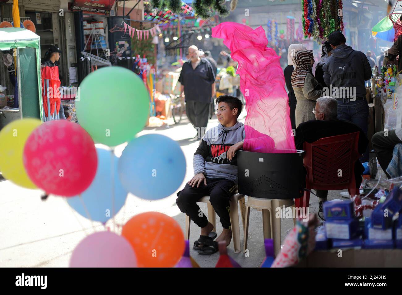 Un garçon palestinien est assis devant la boutique de son père dans le plus ancien marché populaire appelé Al-Zawya dans la ville de Gaza. Les Palestiniens se préparent avant le mois Saint du Ramadan en faisant du shopping dans le plus ancien marché populaire appelé Al-Zawya, au milieu de la ville de Gaza, malgré le prix élevé des marchandises en général causé par l'invasion russe de l'Ukraine. Les musulmans jeûnent au cours du mois du Ramadan, considéré comme l'un des piliers de l'Islam, dans lequel les musulmans s'abstiennent de manger et de boire jusqu'au coucher du soleil. Banque D'Images