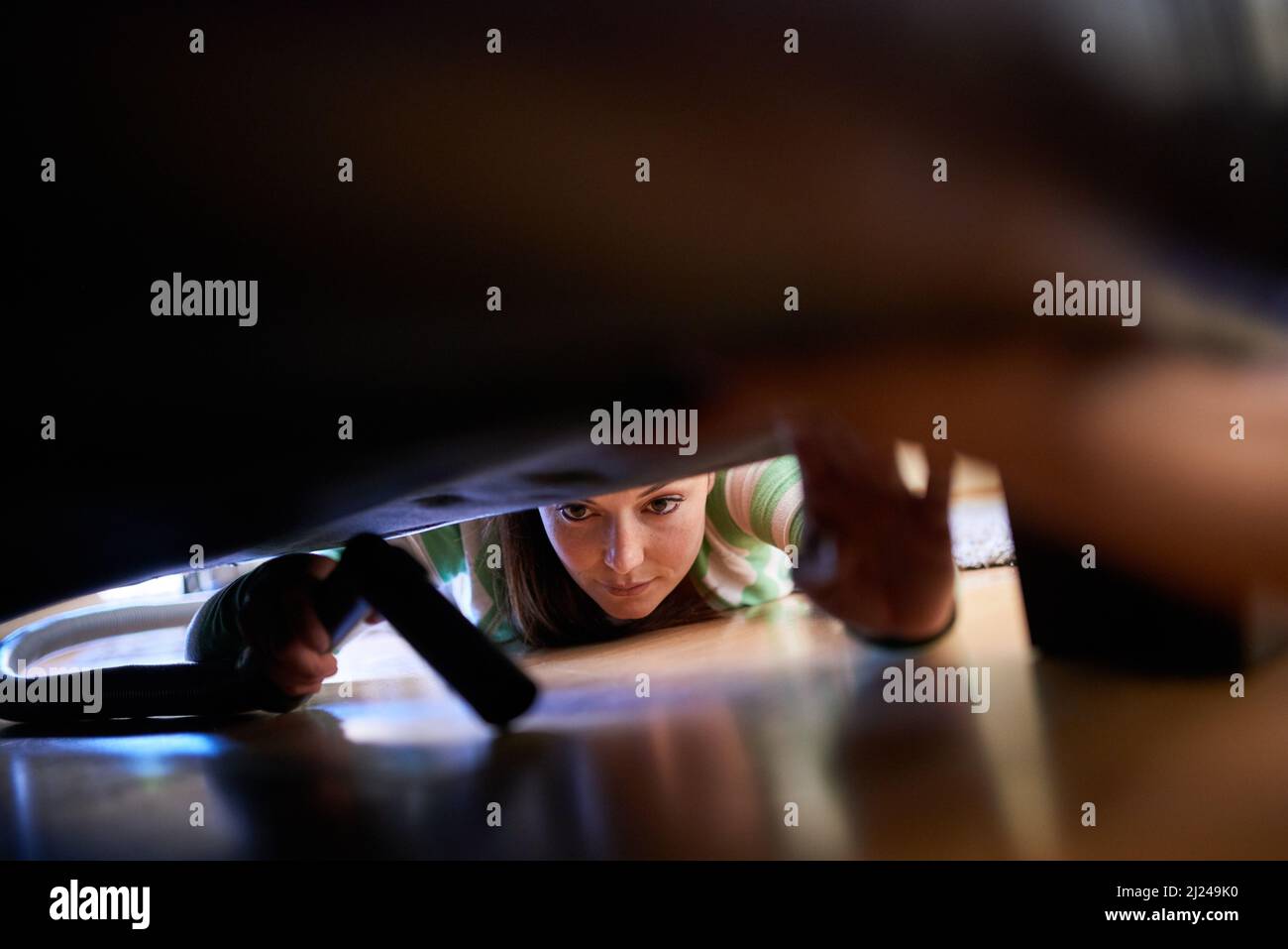 Elle ne manque jamais une place. Photo d'une jeune femme passant l'aspirateur sous un meuble. Banque D'Images