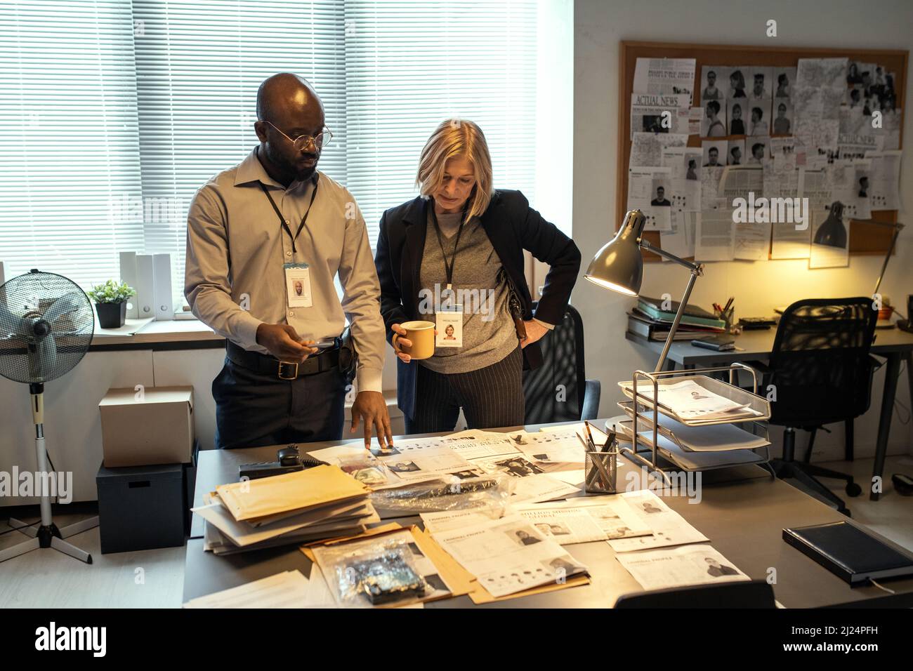 Deux agents interraciaux du FBI formulant des suggestions sur la recherche de chef de gang tout en regardant à travers les données personnelles des criminels Banque D'Images