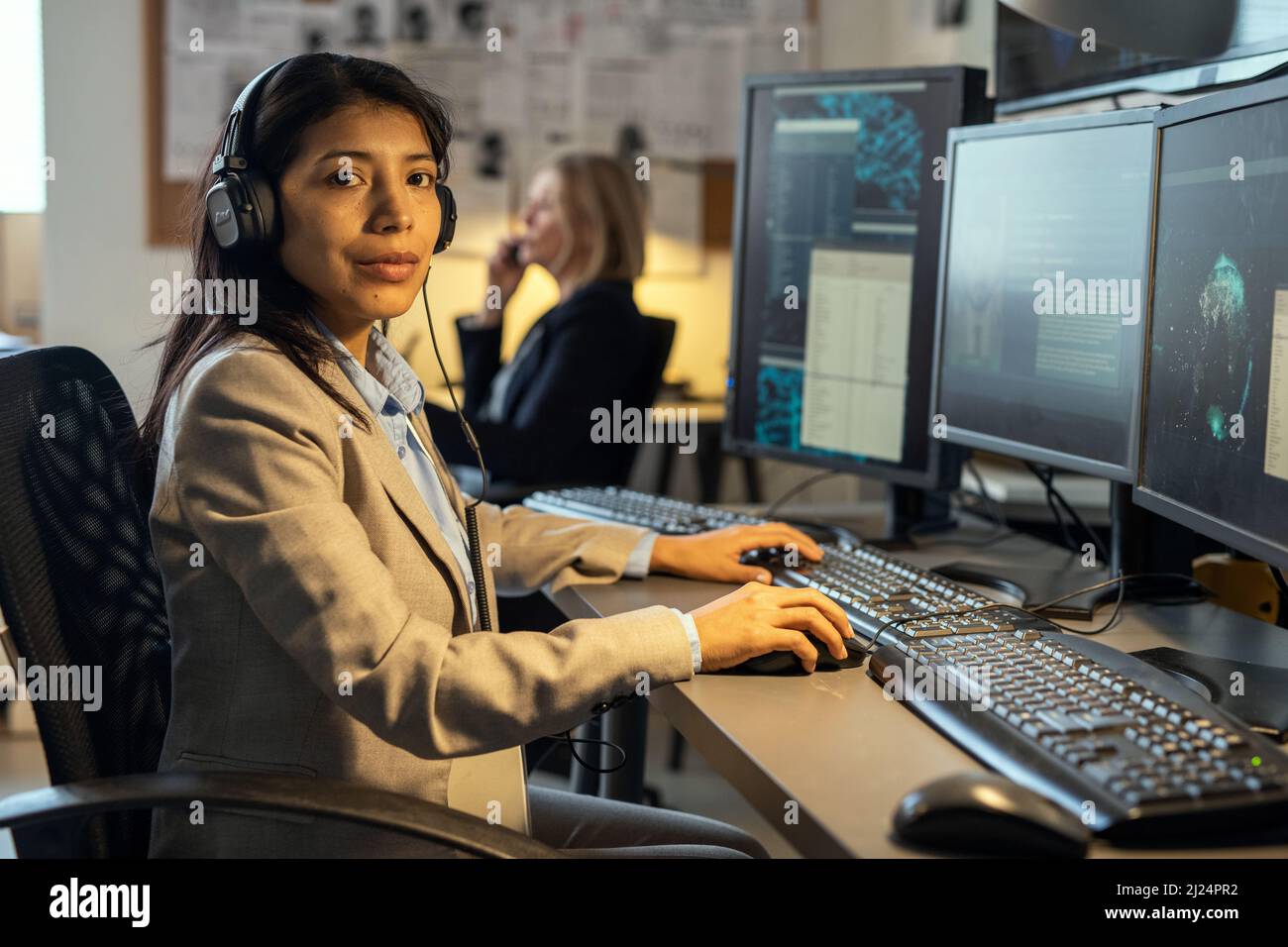 Jeune femme hispanique confiante de service secret avec casque regardant la caméra pendant le travail au bureau Banque D'Images
