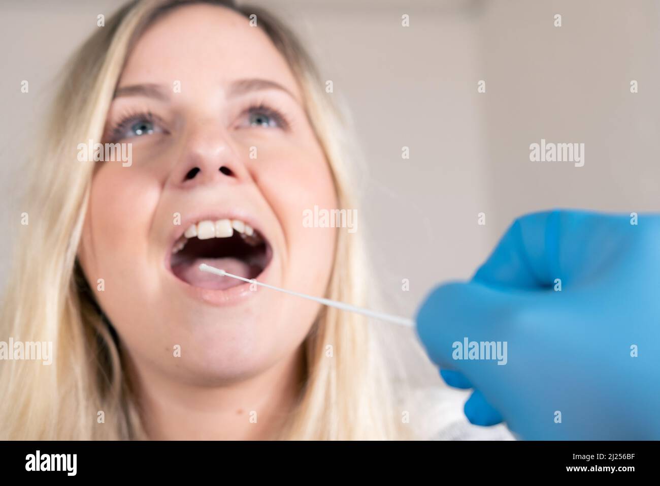 Jolie femme blonde prenant un test Covid-19 / SARS-CoV-2 pendant la pandémie de Corona - médecins gants médicaux bleus en premier plan Banque D'Images