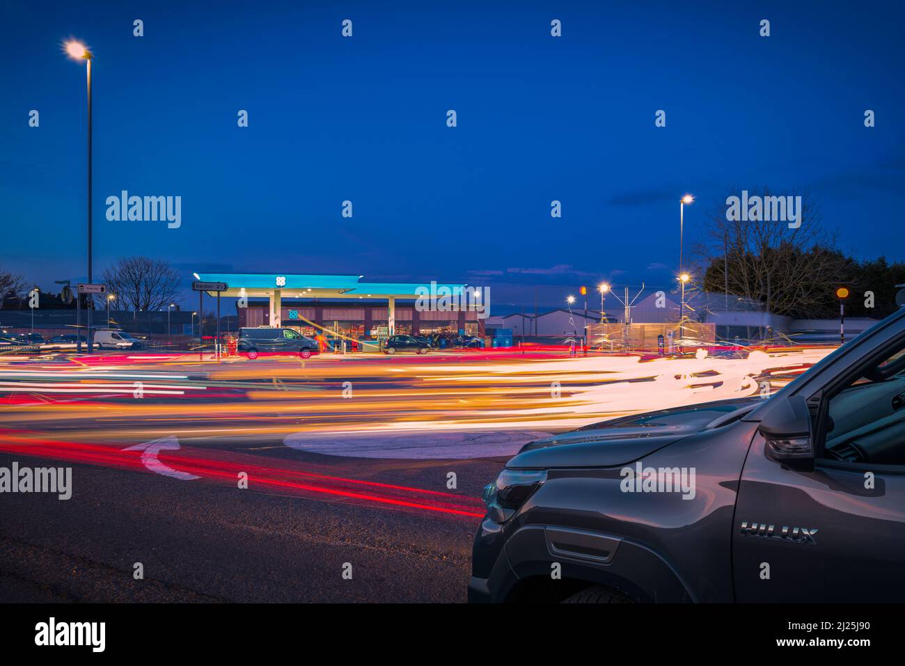 Le trafic aux heures de pointe arrondit un rond-point en face d'une station-service Co-op. Banque D'Images