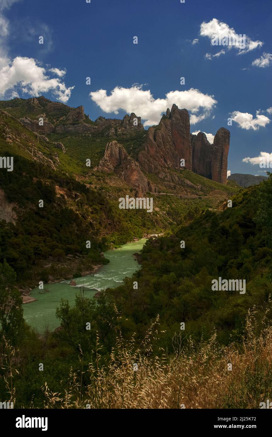 Les ombres nuages assombrissent les pentes accidentées au-dessus des eaux vert clair du Rio Gallego, tandis qu'il s'élève sous les majestueux Mallos de Riglos, une passerelle naturelle spectaculaire vers les Pyrénées. Los Mallos (les maillets), dans la province de Huesca, Aragon, Espagne, ont au moins 20 millions d'années. Ils s'élèvent à environ 300 m (980 pi), formant une frontière physique entre les contreforts pyrénéens et le bassin de l'Ebre. Banque D'Images