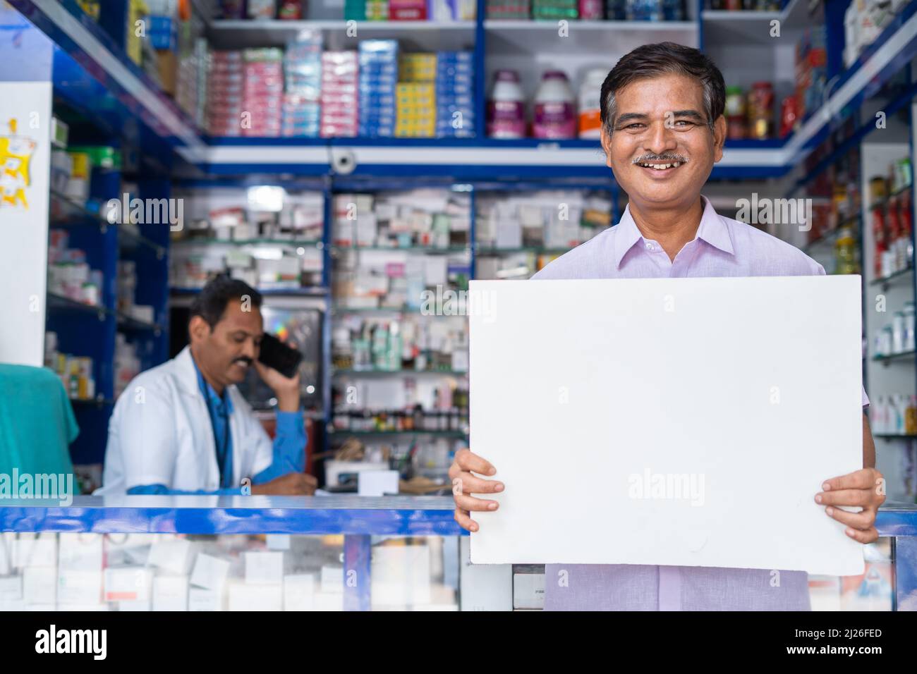 client heureux sytanding en face de la boutique médicale en tenant blanc panneau vide en regardant la caméra - concept de promotion, publicité Banque D'Images
