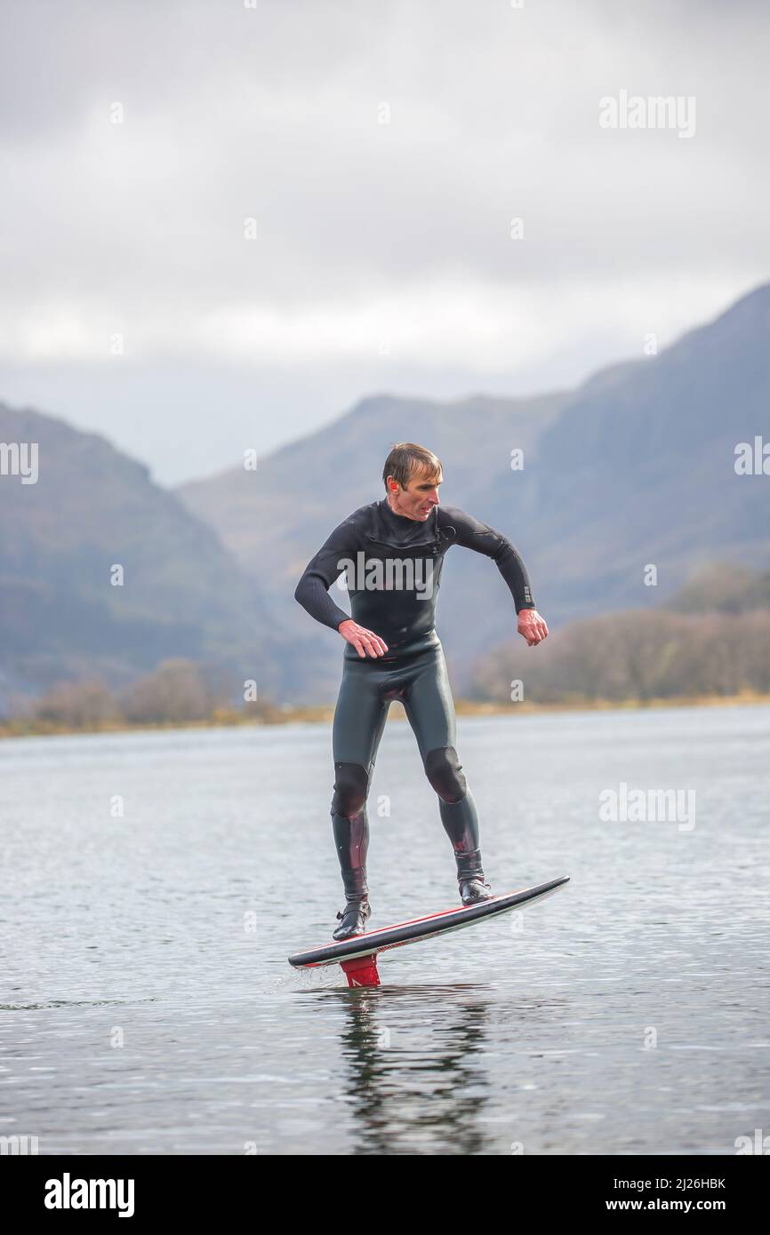 Vue de face d'un homme isolé sur un lac gallois (Llyn Padarn) portant une combinaison, en équilibre dans l'eau sur un hydrofoil. Banque D'Images