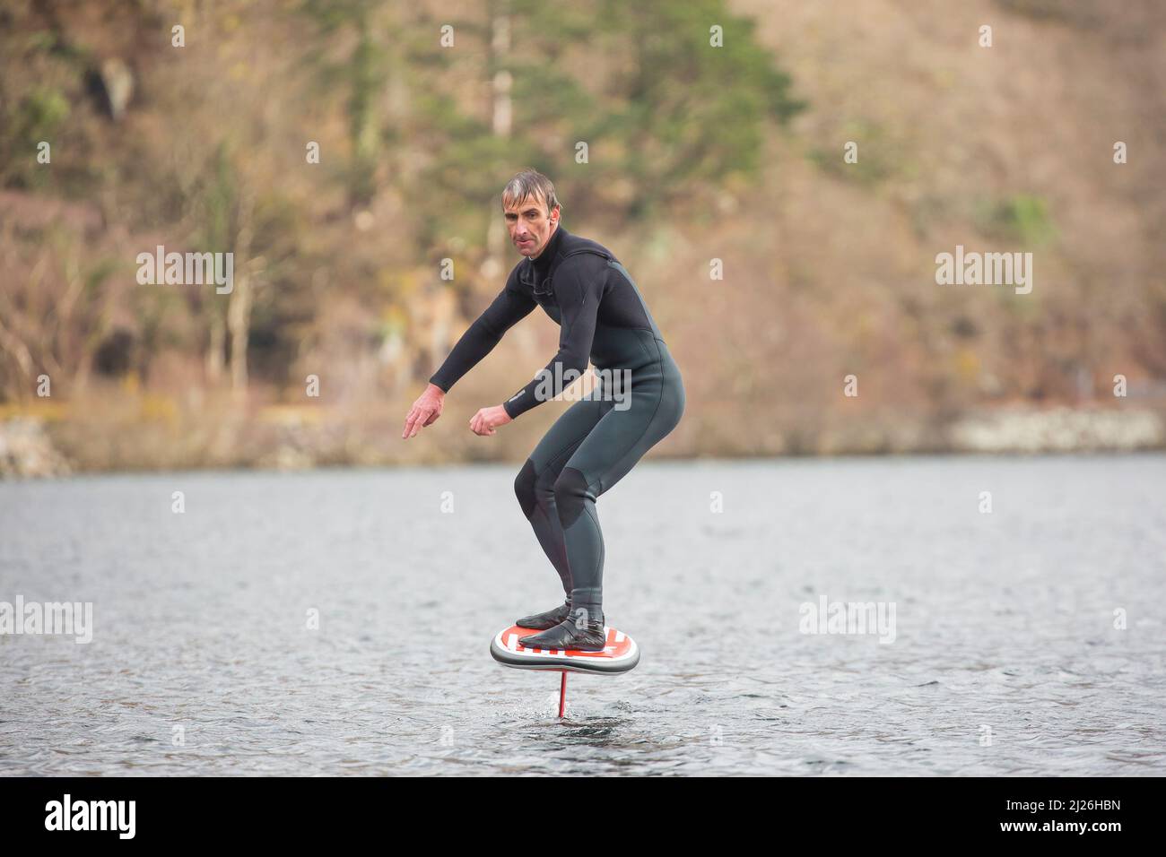 Gros plan de surfeur en combinaison isolée sur un lac gallois (Llyn Padarn), en profitant des sports nautiques, en équilibrant dans l'eau sur une planche hydroptère. Banque D'Images