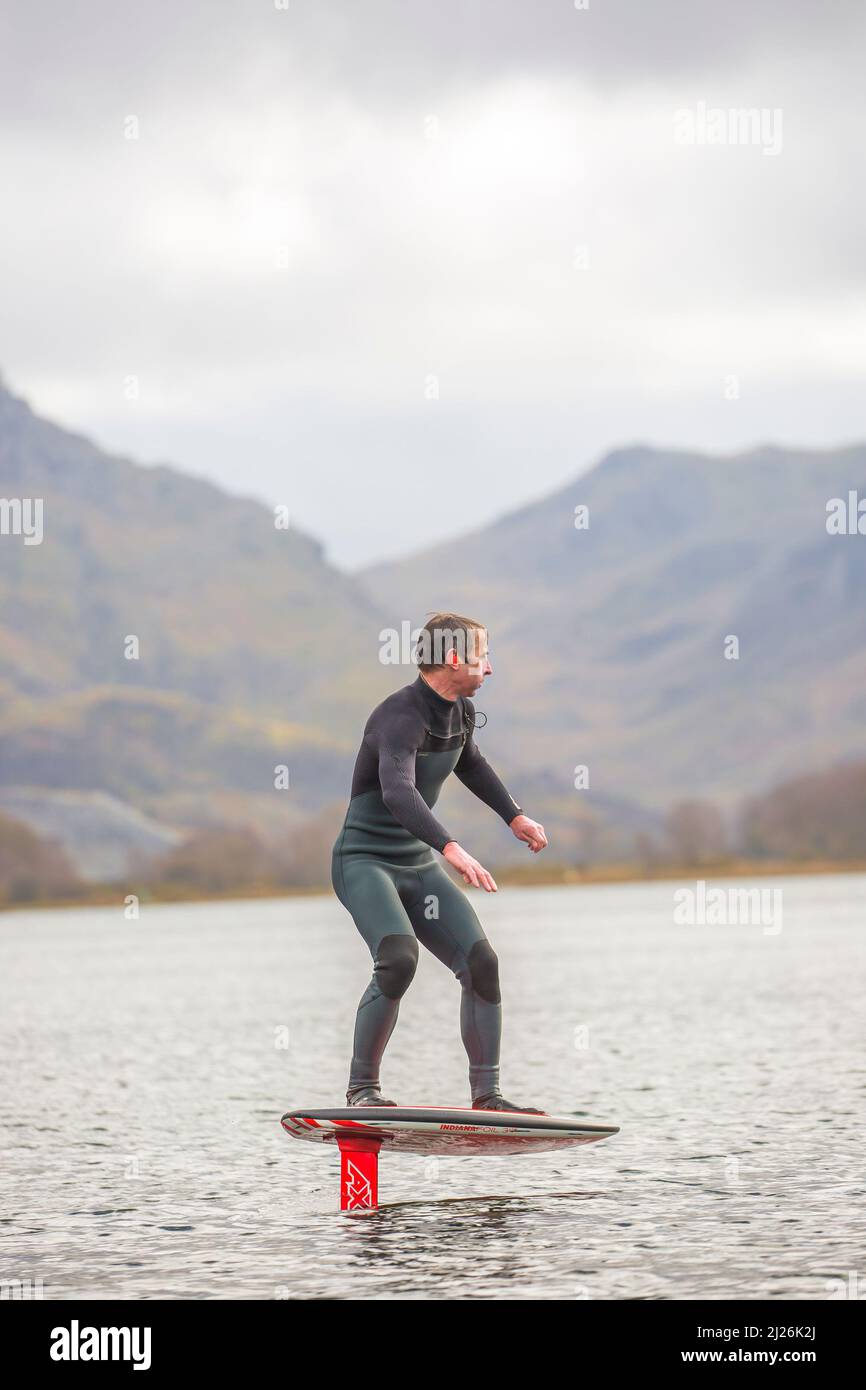 Vue de face d'un homme isolé sur un lac au pays de Galles (Llyn Padarn) portant une combinaison, en équilibre dans l'eau sur un hydroptère. Banque D'Images