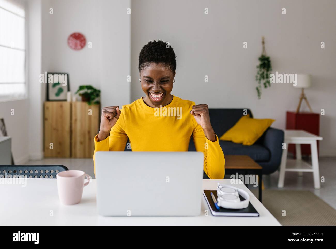 Une jeune femme africaine excitée qui célèbre son succès tout en travaillant sur un ordinateur portable à la maison. Banque D'Images