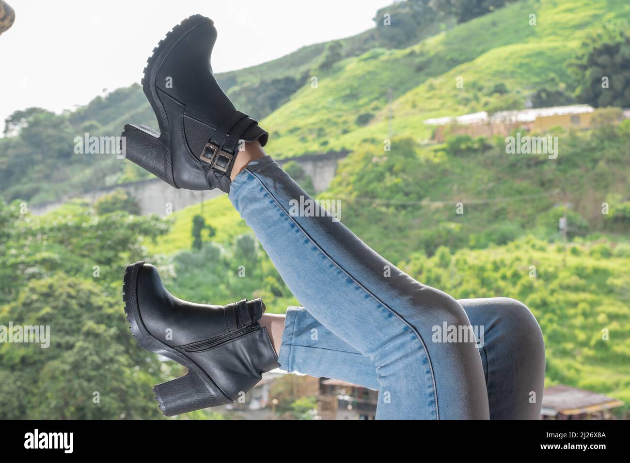 latina fille avec jeans bleus et bottines allongé sur un balcon, levant ses  pieds dans l'air, dans l'arrière-plan un beau paysage rural vert de th  Photo Stock - Alamy