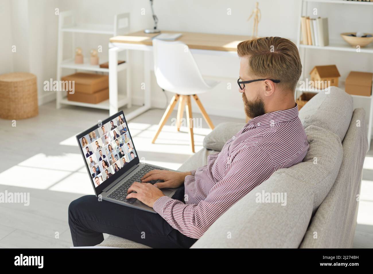 Homme assis sur un canapé dans le bureau à domicile et ayant une réunion d'équipe à distance via conférence téléphonique sur ordinateur portable Banque D'Images