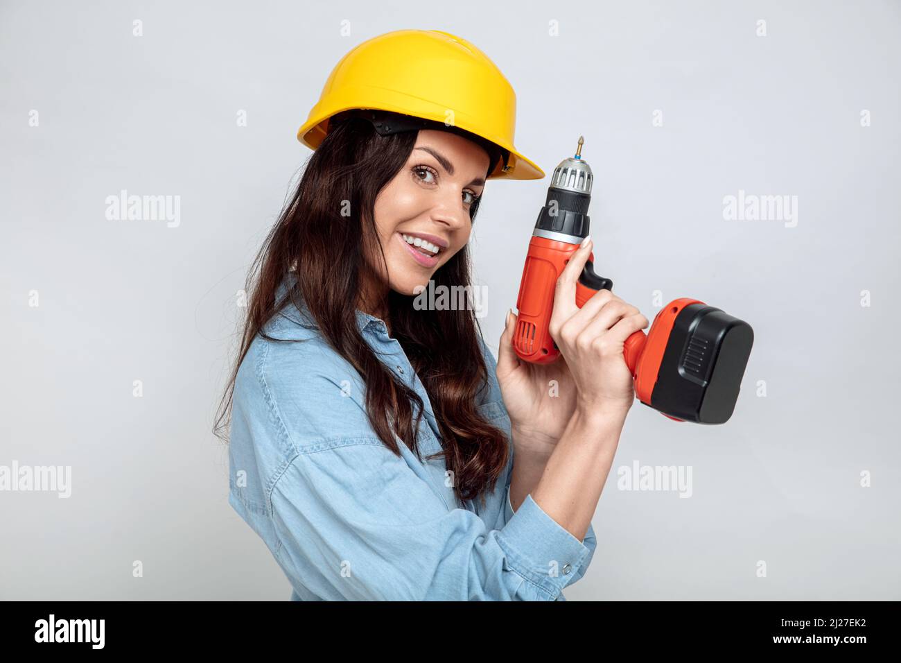 Jeune brune attrayante avec une perceuse électrique et un casque jaune Banque D'Images