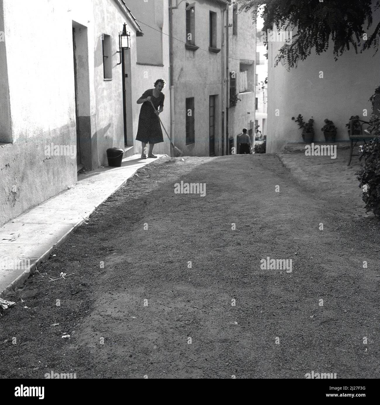 1950s, historique, Italie, une dame balayant sur un chemin de gravier à l'extérieur de sa maison de village. Banque D'Images