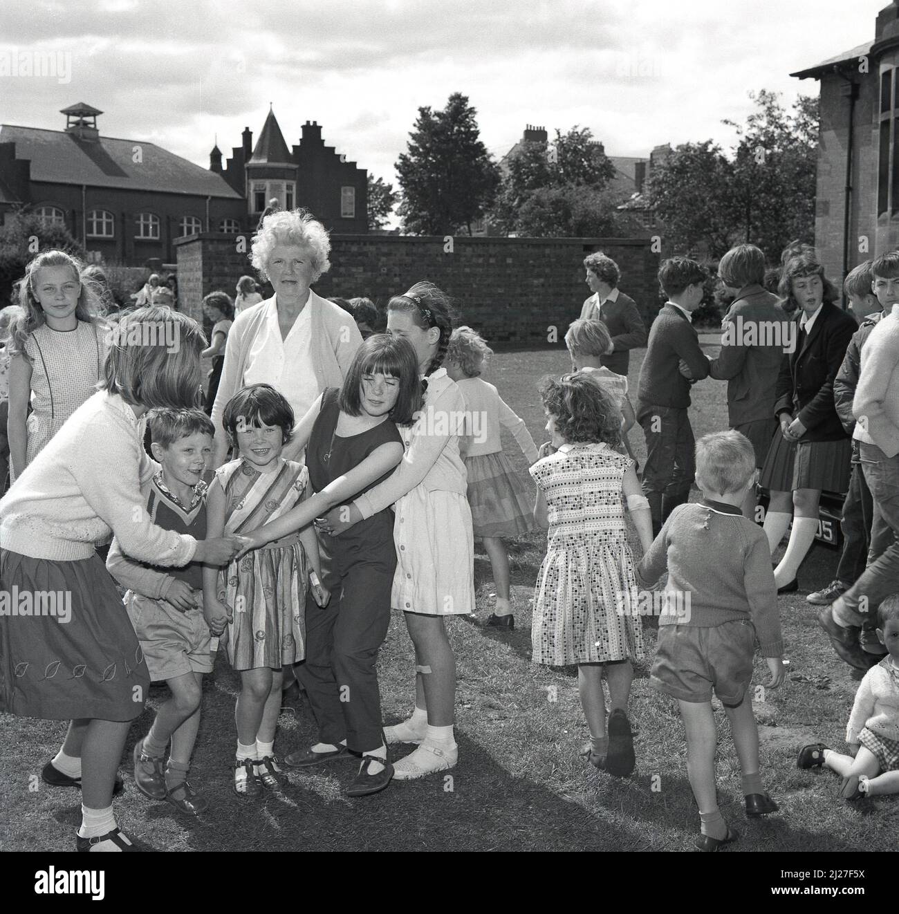1960s, historique, à l'extérieur dans le domaine d'une école primaire, Et les enfants plus âgés jouant un jeu avec des enfants plus jeunes lors d'une fête d'été, Fife, Écosse, Royaume-Uni. Le jeu est connu sous le nom de « oranges et citrons », où les enfants se déplacent ou dansent à travers une arche faite par des enfants tenant les mains, face à face, les bras levés. Il est également connu sous le nom de « London Bridge is Falling down ». Banque D'Images