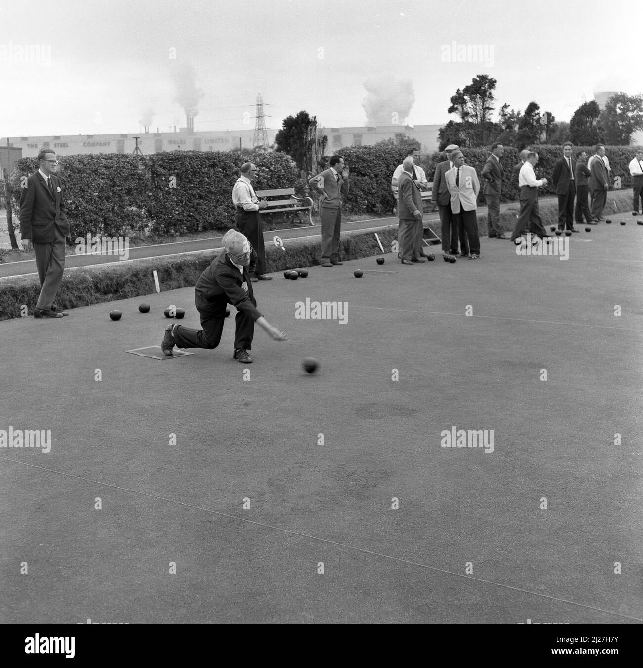 1950s, historcal, les hommes jouant des boules de vert de couronne au club de bowling de l'usine d'acier à Abbey Works, pays de Galles, Royaume-Uni, le nom de la compagnie d'acier du pays de Galles limitée et les cheminées de ses usines peuvent être vus au loin. Banque D'Images