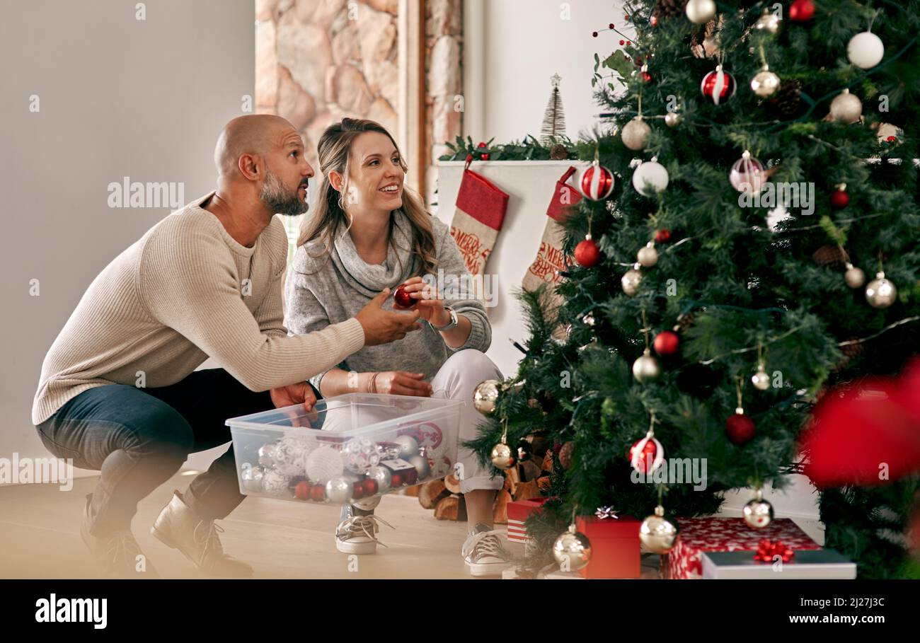 Vous pouvez mettre celui-ci vers le haut. Coupe courte d'un couple joyeux d'âge moyen, mettant des décorations sur un arbre de Noël à l'intérieur à la maison pendant la journée. Banque D'Images