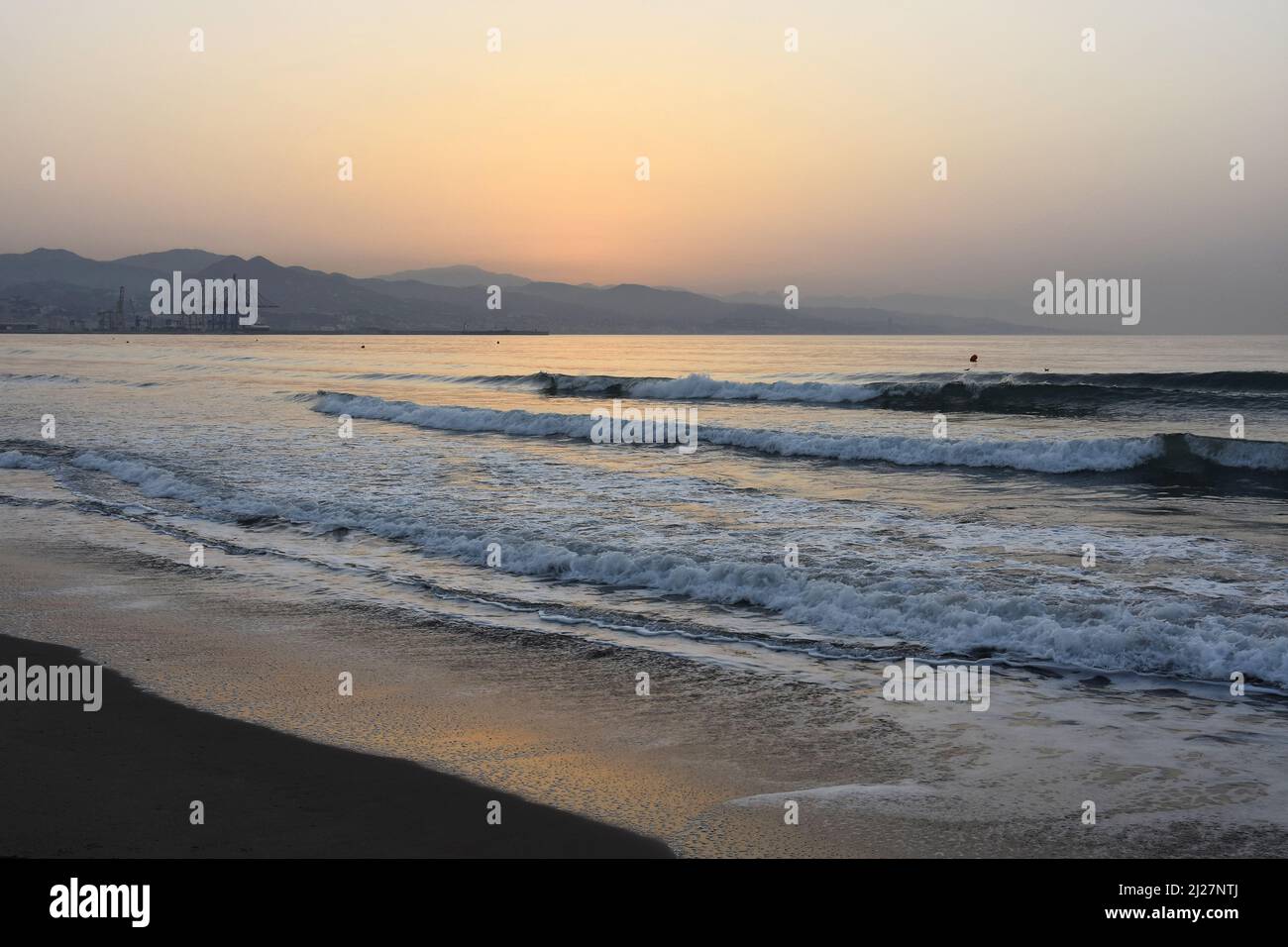 Vagues approchant la côte de Malaga à l'aube avec port industriel en arrière-plan, Costa del sol Andalousie sud de l'Espagne. Banque D'Images