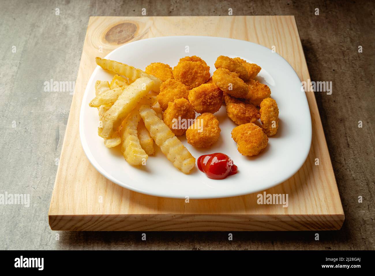 Nuggets de poulet et frites avec un peu de sauce tomate sur une assiette sur une surface en bois, prêts à manger, repas rapide Banque D'Images
