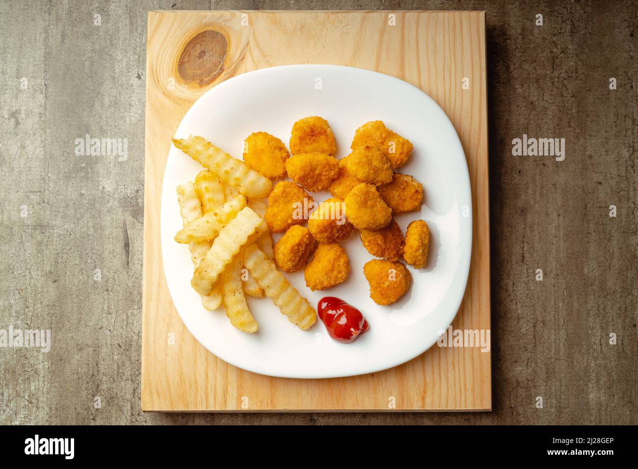 Nuggets de poulet et frites avec un peu de sauce tomate sur une assiette sur une surface en bois, prêts à manger, repas rapide Banque D'Images
