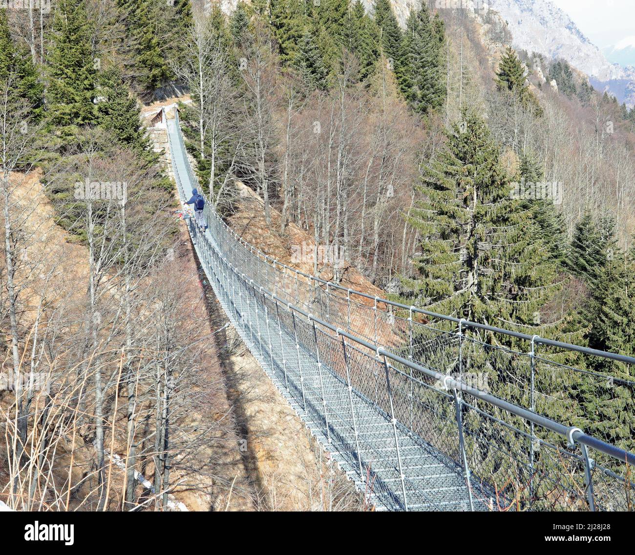 Long pont tibétain reliant les rives des crêtes de montagne en hiver et une personne la traversant Banque D'Images