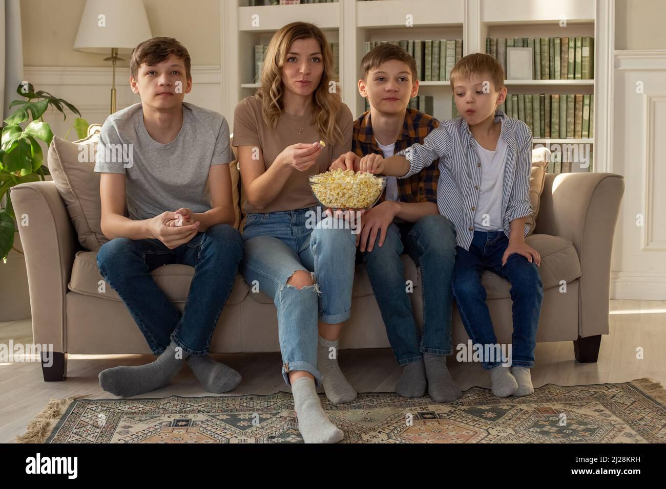 Une famille heureuse, une femme et trois garçons, sont assis sur le canapé dans le salon avec un bol de pop-corn, regardant la télévision Banque D'Images