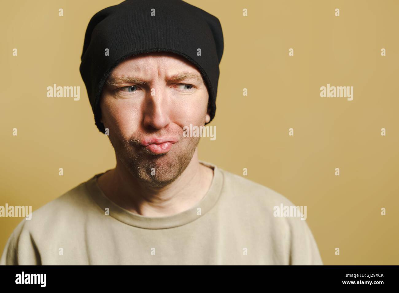 L'homme dans le chapeau noir regarde avec mépris. Portrait d'un jeune homme faisant des visages. Banque D'Images