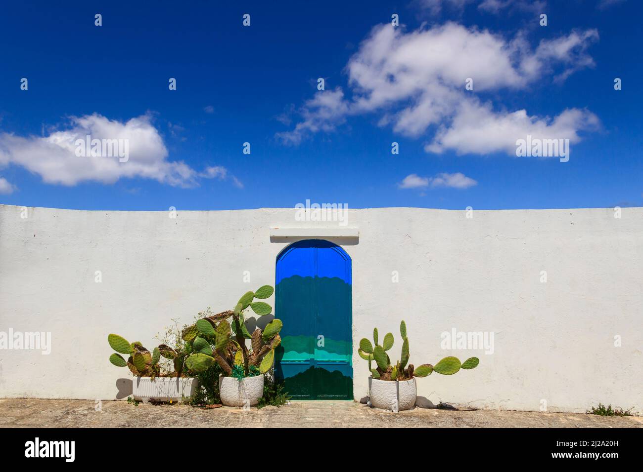 Ciel bleu avec nuages, porte bleue avec poire piqueuse et mur blanc traditionnel dans la ville d'Ostuni à Apulia, Italie. Banque D'Images