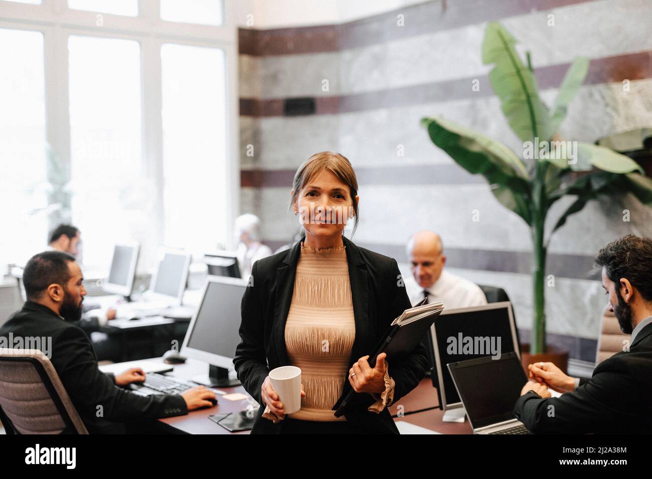 Portrait d'une femme jeune et mûre souriante tenant une tasse à café et des documents au bureau d'avocats Banque D'Images