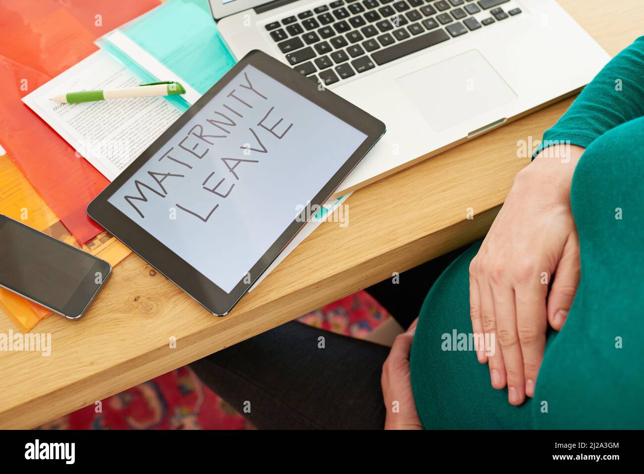 Pas longtemps maintenant Une femme enceinte assise avec un comprimé avec les mots congé de maternité à l'écran. Banque D'Images