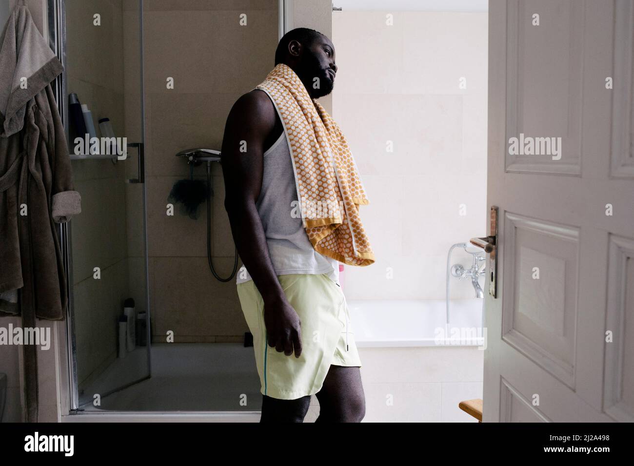 Homme mentalement épuisé avec une serviette penchée sur le mur de la salle de bains à la maison Banque D'Images