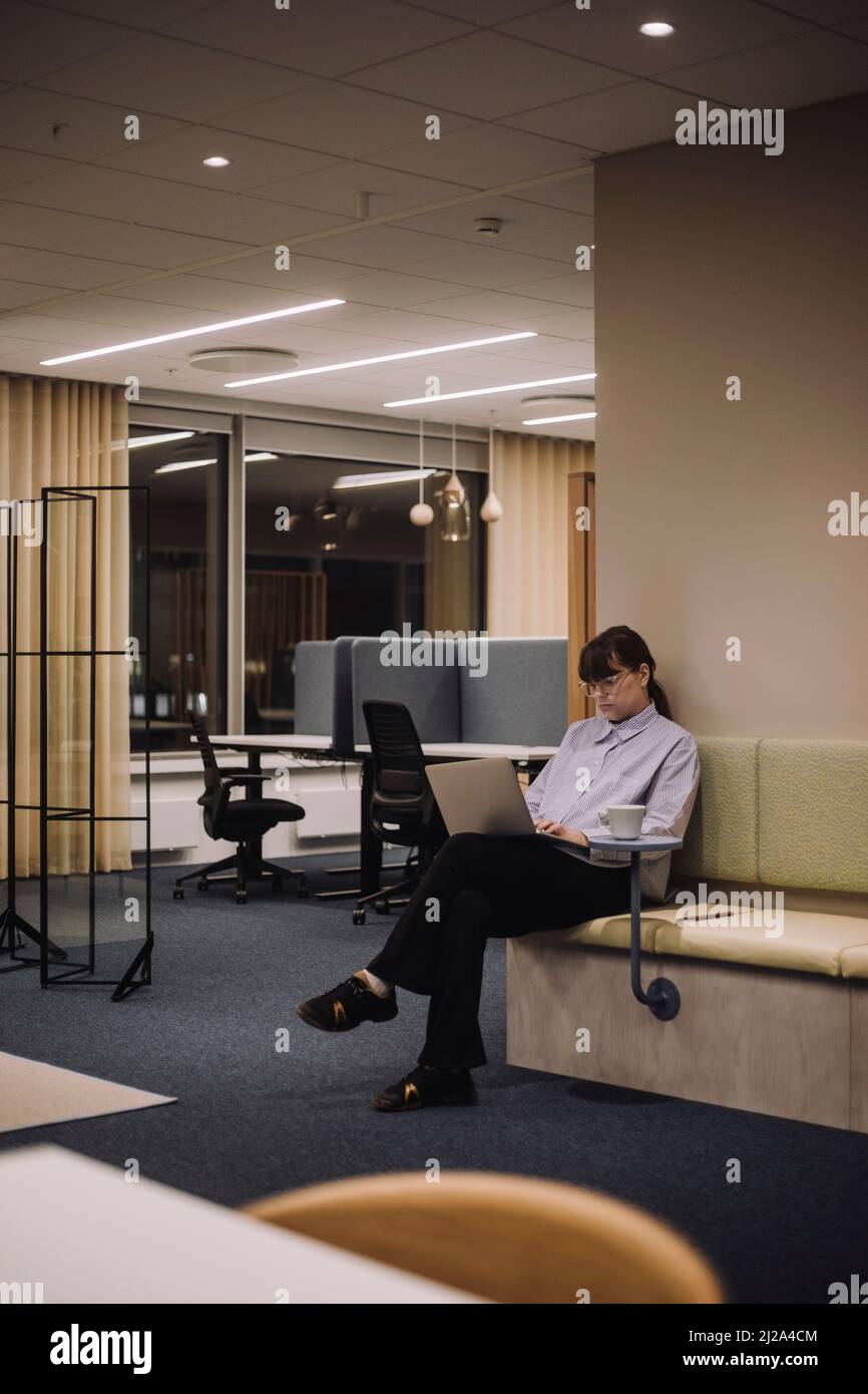 Jeune femme d'affaires utilisant un ordinateur portable tout en travaillant tard sur le lieu de travail Banque D'Images