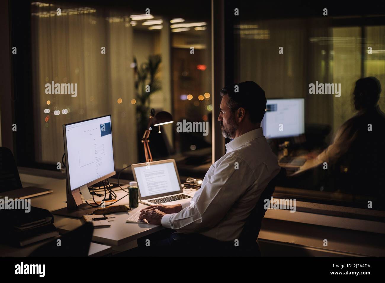 Homme d'affaires tapant sur le clavier de l'ordinateur tout en travaillant dans le bureau la nuit Banque D'Images