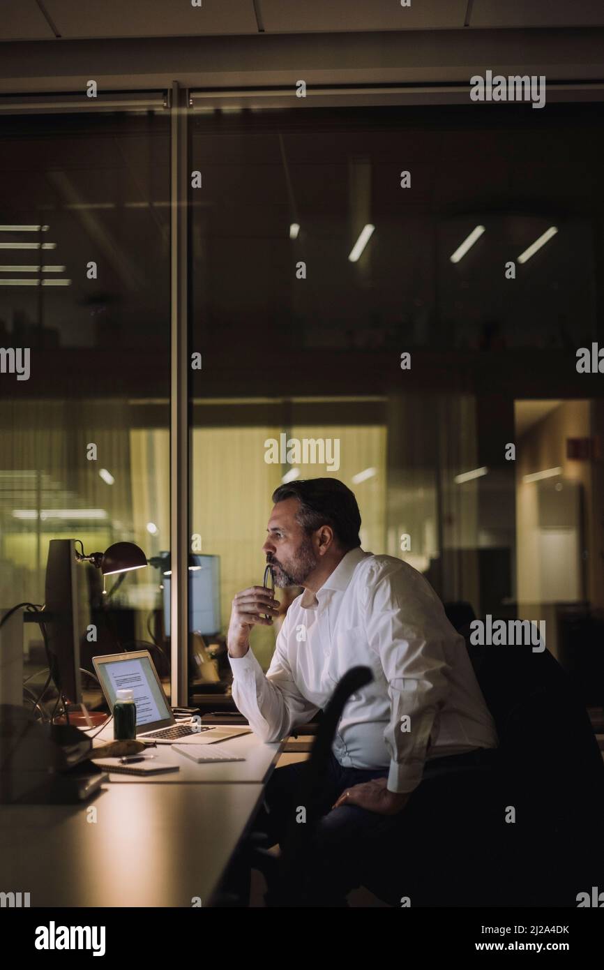 Homme d'affaires mature travaillant sur un ordinateur dans un lieu de travail la nuit Banque D'Images