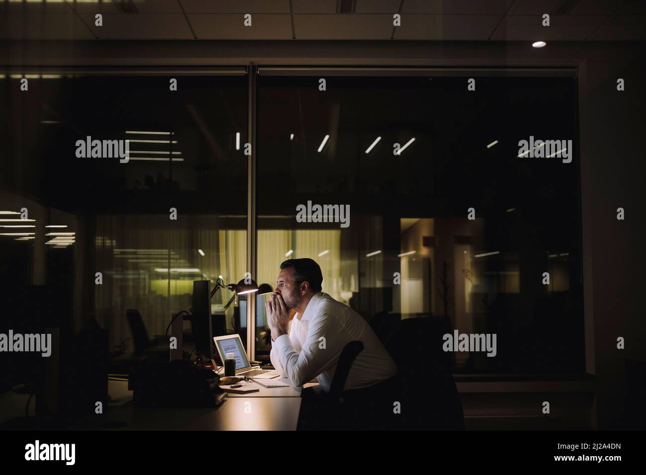 Homme d'affaires se concentrant tout en travaillant des heures supplémentaires au bureau la nuit Banque D'Images